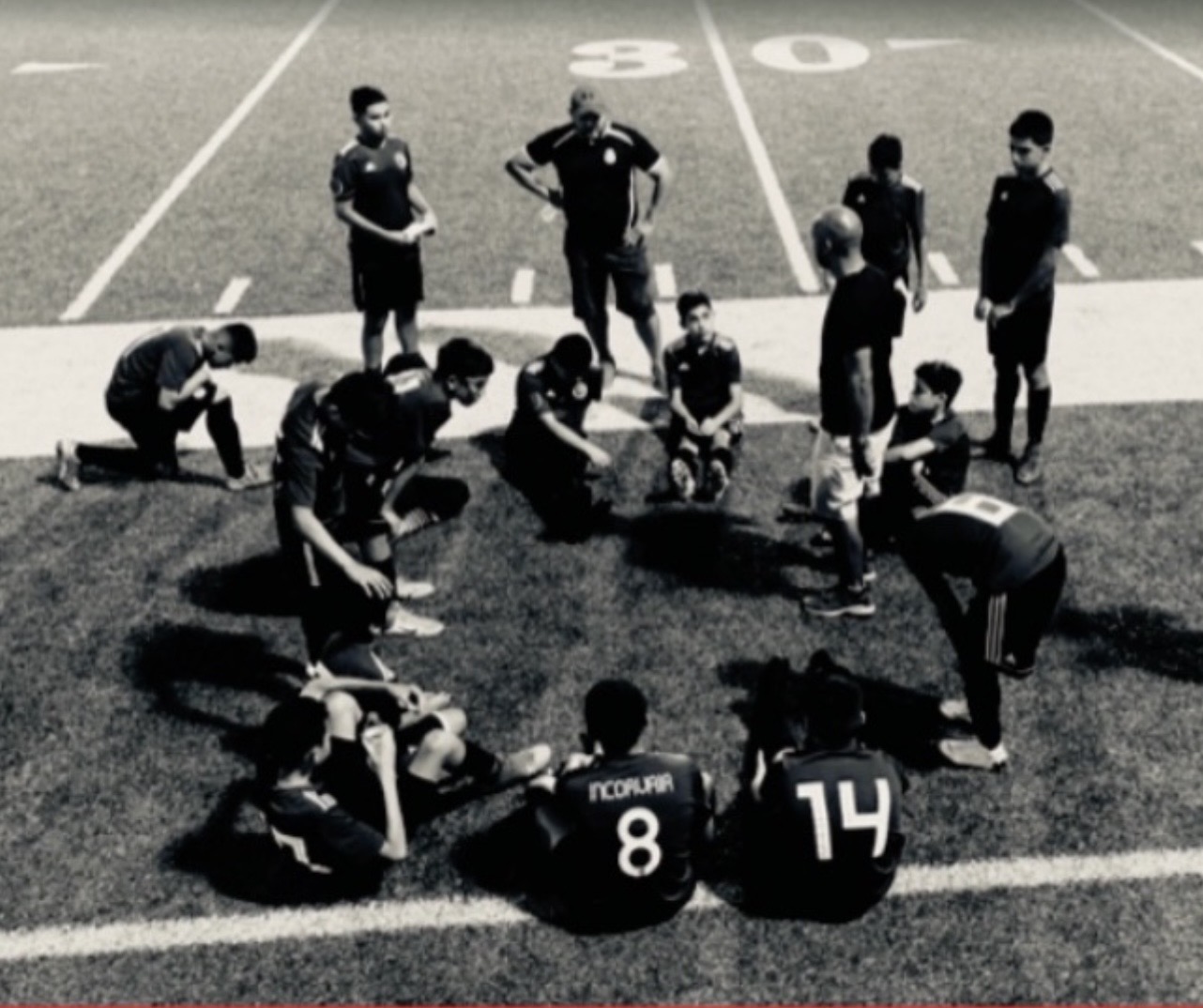 Team gathered in a circle on the field in black and white